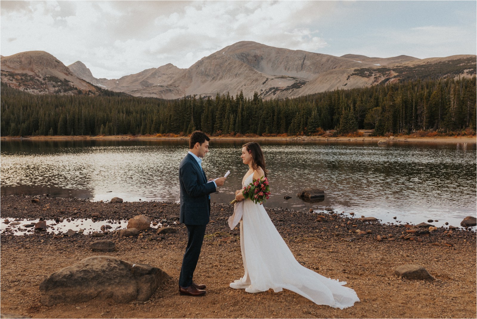 Bride and groom exchanging vows for their elopement in Colorado, standing in front of a lake, with mountains and trees in the distance.