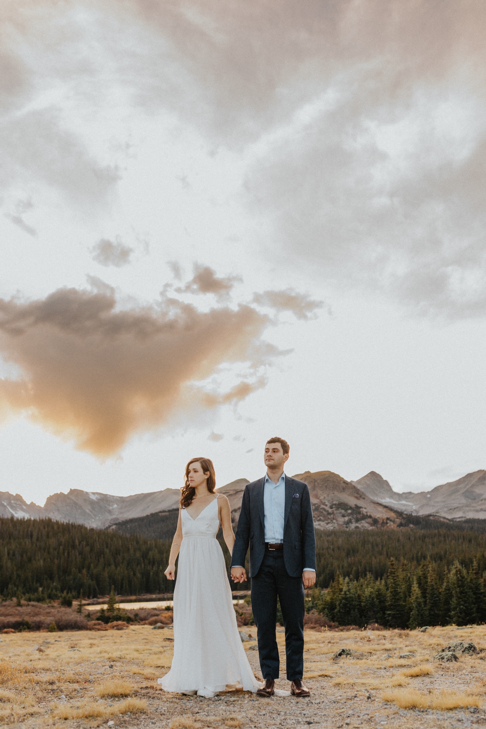 Cinematic image of married couple standing in front of mountains with a sunset sky in the background during their elopement in Colorado.
