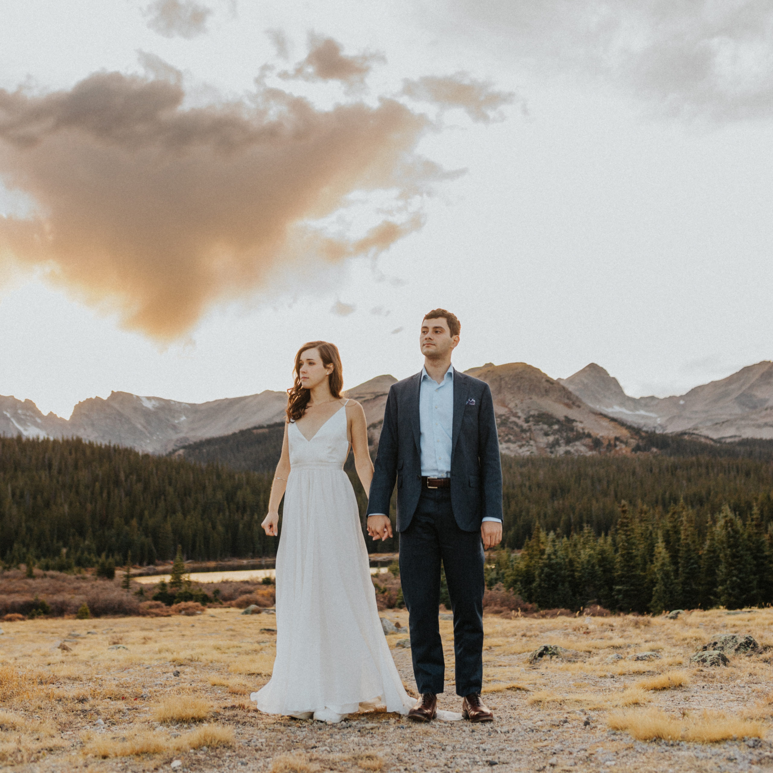 Couple standing in a rolling field with the Rocky Mountains and a lake behind them after their elopement in Colorado.